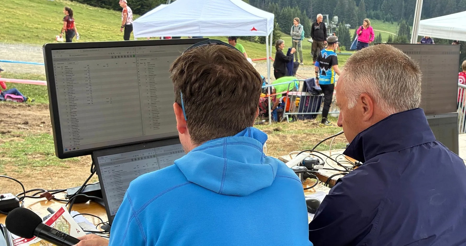 Zwei Männer sitzen vor einem Monitor auf dem Wettkampfergebnisse angezeigt werden. Wettkampfzentrale und Sprecher